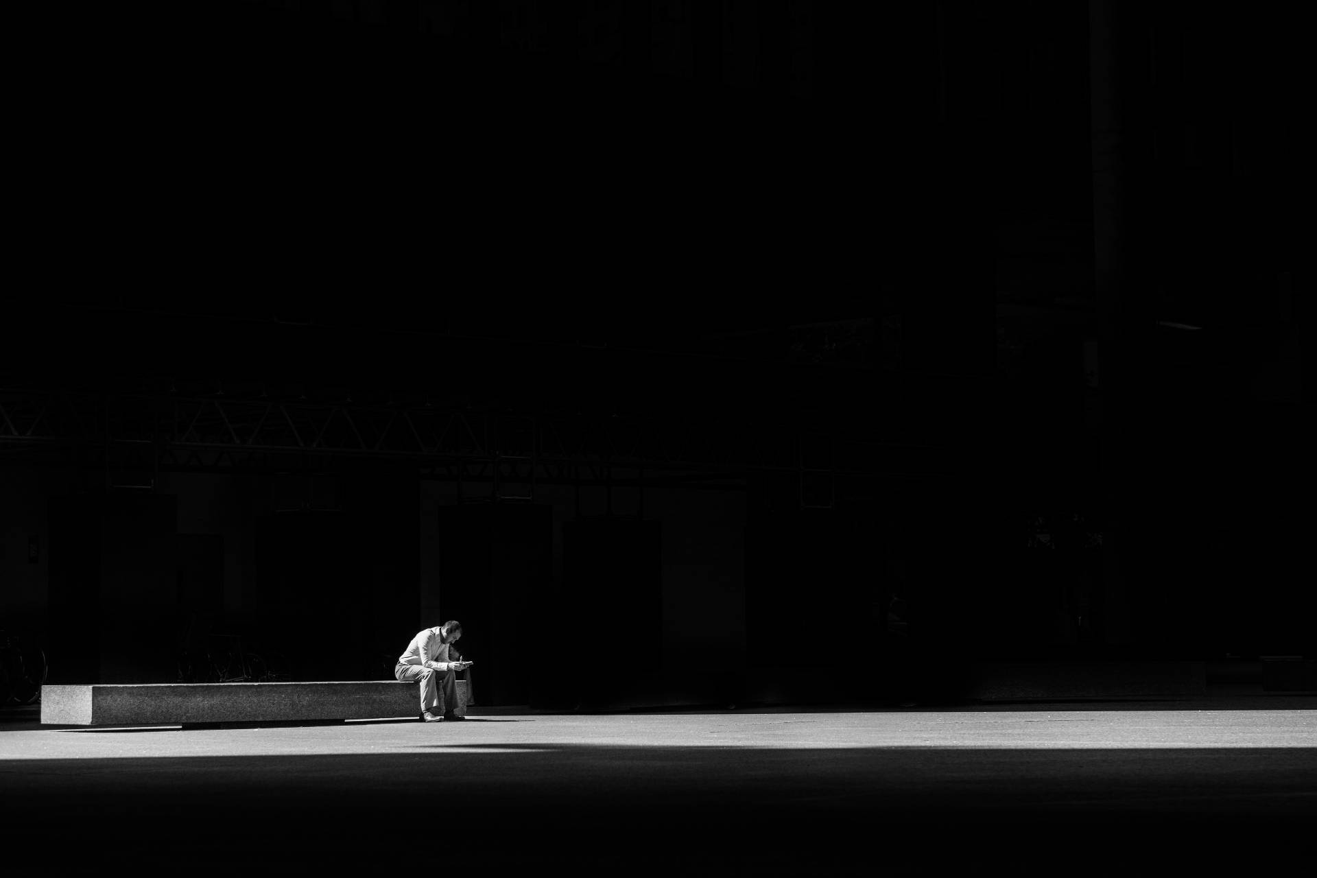 un hombre cabizbajo triste sentado solo en una banco de piedra en la oscuridad ministry of loneliness